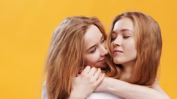 Крупный план портрета двух обнимающихся молодых рыжеволосых сестер-близнецов, наслаждающихся их связью, оранжевый фон студии — стоковое видео