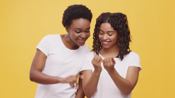 Duas amigas afro-americanas olhando para as unhas e discutindo grande manicure, fundo de estúdio laranja — Vídeo de Stock