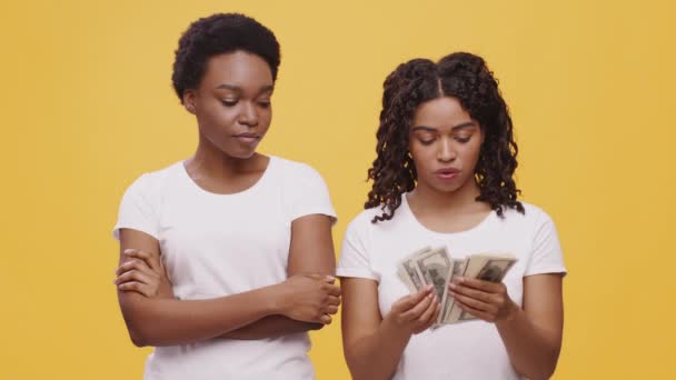 Jong Afrikaans amerikaans vrouw tellen geld en het geven van deel aan haar vrouwelijke partner, oranje studio achtergrond — Stockvideo