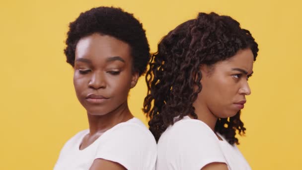 Dos amigas afroamericanas gruñonas paradas espalda con espalda, sintiéndose ofendidas e irritadas, fondo naranja — Vídeos de Stock