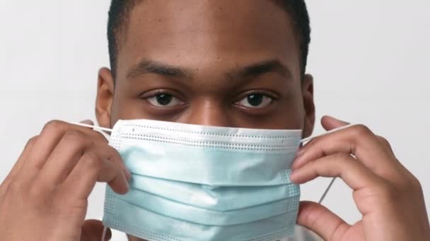Lukk opp portrettet av en ung, afroamerikansk mann som tar på seg beskyttende medisinsk maske, sakte film – stockvideo