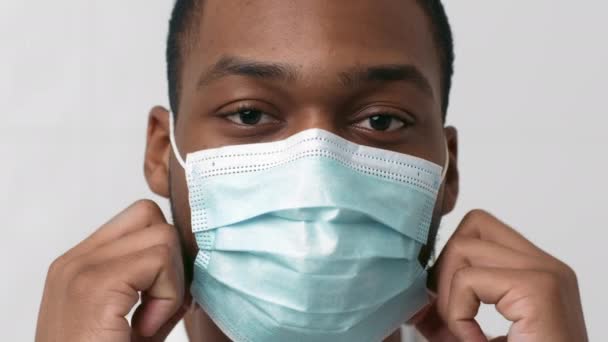 Närbild porträtt av positiv svart kille som tar av skyddande medicinsk mask och ler mot kameran, slow motion — Stockvideo