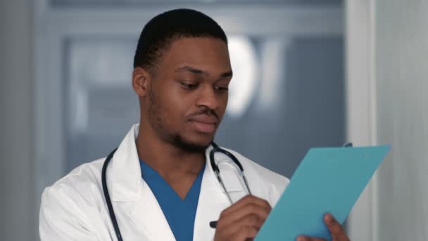 Dokumenty z kliniky. Rušný černošky muž terapeut psaní lékařský předpis ve schránce v nemocnici — Stock video