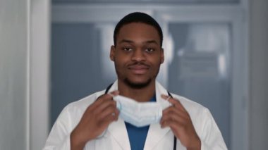 Klinikte çalışmadan önce koruyucu maske takan Afrikalı Amerikalı genç bir doktorun portresi.