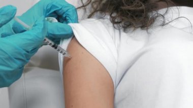 Genç bir kadının klinikteki doktordan koronavirüs aşısı olurken yakın çekim.