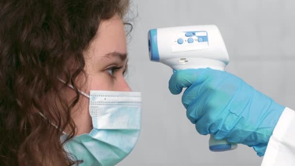 Врач вручает медицинские перчатки, измеряющие температуру пациенток бесконтактным инфракрасным термометром — стоковое видео