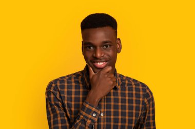 Yakışıklı Afrikalı Amerikalı adam çenesine dokunuyor ve kameraya ilgiyle bakıyor.