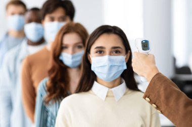 Temassız termometreye sahip kadın. Çok ırklı insanların sıcaklığını ölçüyor.