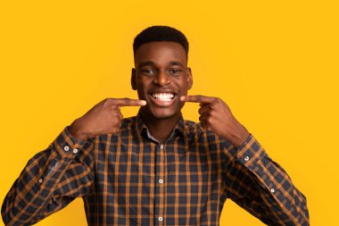 Mükemmel gülümseme. Beyaz dişlerini parmaklarıyla gösteren mutlu siyah adam.
