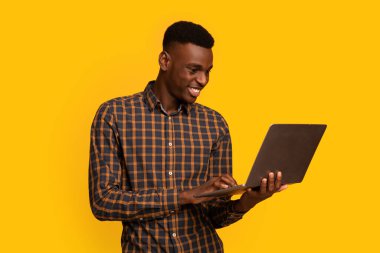 Bağımsız çalışma. Sırıtkan Afrikalı Adam 'ın Sarı Arkaplan Üzerinde Laptop Kullanırken Portresi