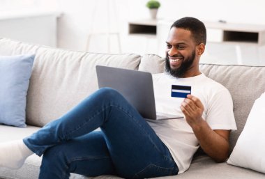 Siyah adam dizüstü bilgisayar ve kredi kartı kullanıyor. İnternetten alışveriş yapıyor.
