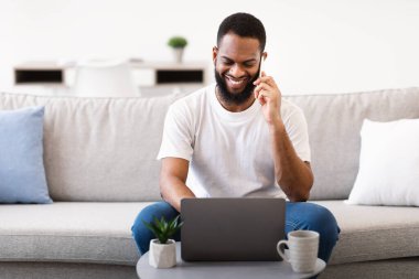 Laptop 'ta cep telefonuyla konuşan mutlu siyah serbest çalışan adam.
