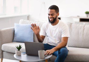 Siyah adam laptopta video görüşmesi yapıyor. Evde oturuyor.