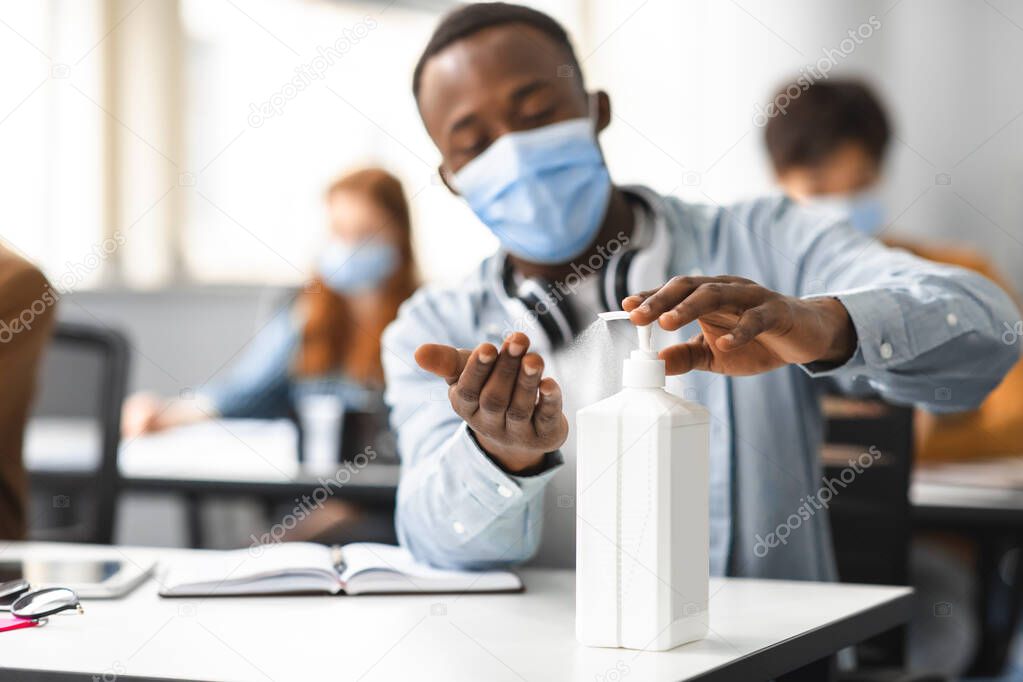Afro male student applying antibacterial sanitizer on hands