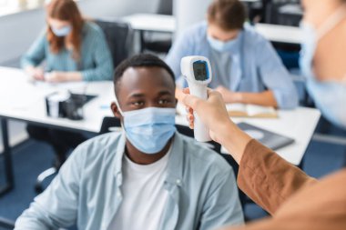 Temassız termometresi olan, öğrencinin sıcaklığını ölçen, seçici odaklı bir kadın.