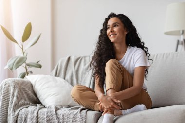 Evdeki kanepede oturan neşeli genç bayan.