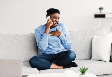 Siyahi kadın arkadaşını arıyor, kanepede oturuyor.