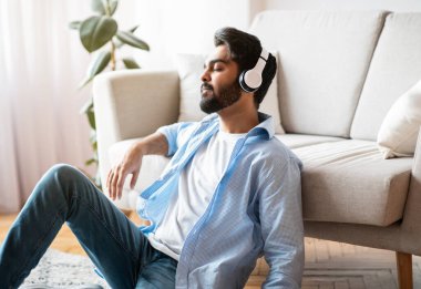 Rahatlama zamanı. Evde müzik dinleyen kulaklıklı sakin bir Arap.