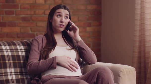 Χαρούμενη έγκυος γυναίκα που μιλάει στο κινητό, ξεκουράζεται στο σπίτι και χαϊδεύει την κοιλιά της, αργή κίνηση — Αρχείο Βίντεο
