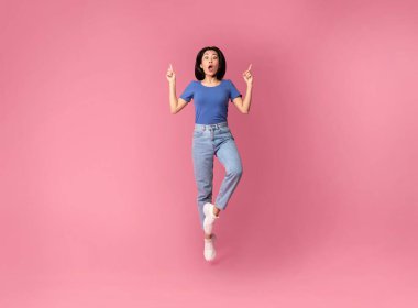 Şaşkın Asyalı genç kadın zıplıyor ve işaret ediyor.