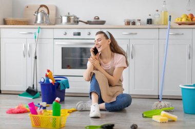 Genç ve mutlu ev hanımı mutfakta akıllı telefondan konuşuyor, ev işlerine ara verip arkadaşınla konuşuyor.