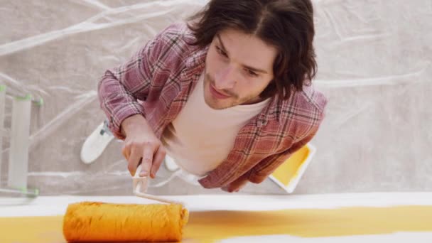 Hoge hoek uitzicht op jonge man schilderen muur met gele verf op rol, glimlachen op de camera — Stockvideo