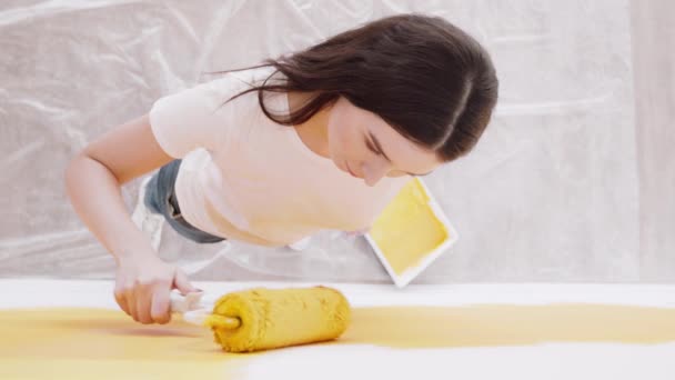 Renovación del hogar. Joven mujer concentrada pintando pared con tinte amarillo, trabajando con rodillo, vista superior — Vídeo de stock