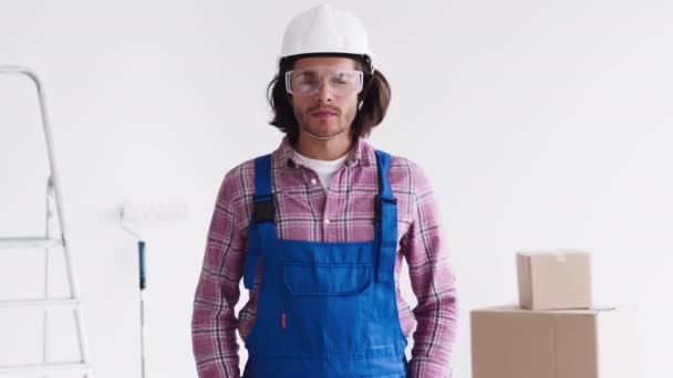 Zelfverzekerde renovatie klusjesman in uniform met beschermende bril en helm kijkend naar camera — Stockvideo