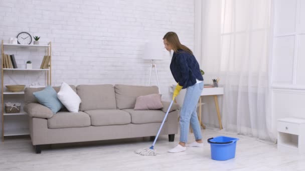 Καθαρισμός. Νεαρή νοικοκυρά καθαρισμού δαπέδου στο σπίτι με σφουγγαρίστρα και κουβά, φορώντας γάντια από καουτσούκ — Αρχείο Βίντεο