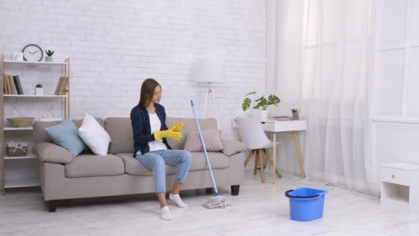 Trøtt ung husmor som hviler på sofaen, endelig ferdig med vårrengjøringen hjemme, tar av gummihansker – stockvideo