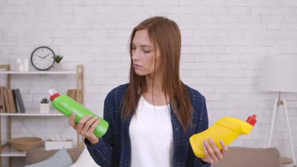Fiatal töprengő nő kezében két üveg mosószer, olvasási összetétel és válasszon egy otthoni takarítás — Stock videók