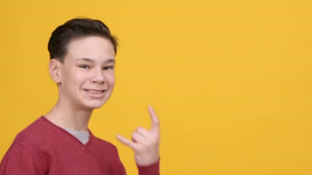 Забавный мальчик-подросток, говорящий на языке рок-сигнала, на желтом фоне — стоковое видео