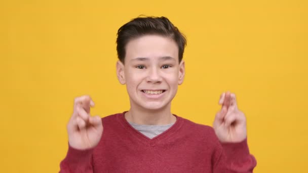 Мальчик держит пальцы скрещенными на удачу на жёлтом фоне — стоковое видео