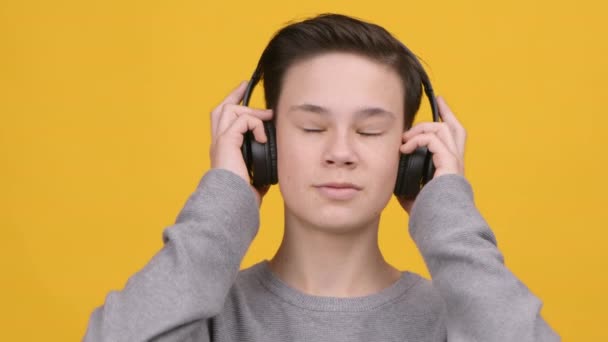 Ragazzo ascolto di musica online indossando cuffie wireless, sfondo giallo — Video Stock