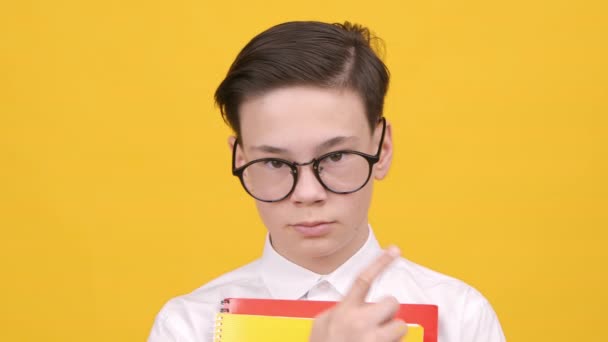 Colegial ajustando anteojos sosteniendo libros posando sobre fondo amarillo — Vídeo de stock