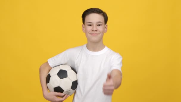 Teen Boy holding Soccer Ball Gesturing hüvelykujj-up felett sárga háttér — Stock videók