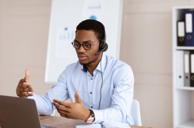 Afro-Amerikalı adamın bilgisayarla, ofis içi bilgisayarla görüntülü görüşmesi var.