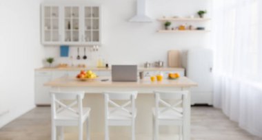 Laptop ve meyveler masada, çatal bıçaklı beyaz mobilyalar, sandalyeler, tabaklar ve saksılarda bitkiler.