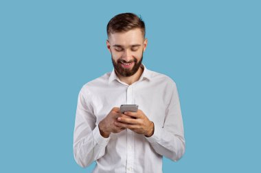 Genç adam akıllı telefon ekranına bakıyor, internette geziniyor, online oyun oynuyor, mavi arka planda alışveriş yapıyor.