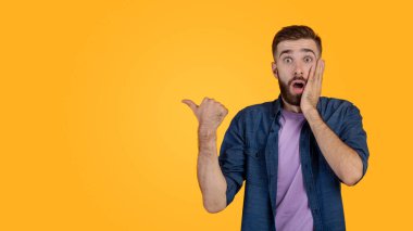 Terfi konsepti. Sersemlemiş hipster adam boş alanı işaret ediyor, turuncu stüdyo hakkında bir şeyler öneriyor.