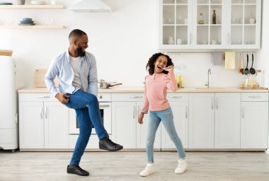 Siyah baba ve kızı birlikte yemek yaparken şarkı söyleyip dans ediyorlar.