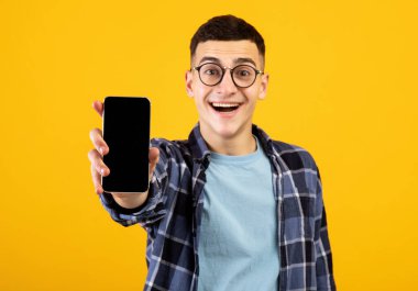 Turuncu arka planda boş ekranlı cep telefonu gösteren mutlu genç adam, mobil uygulama veya web sitesi tasarımı için model