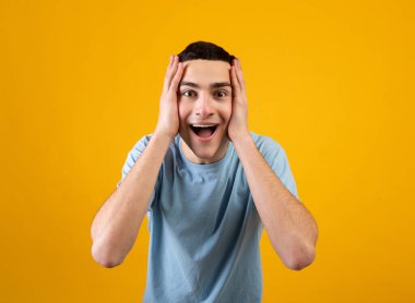 İnanılmaz bir tanıtım. Turuncu stüdyo arka planında kafası şokta olan yakışıklı bir genç.