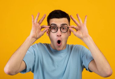 Milenyum adamı gözlüklerine dokunup turuncu stüdyo arka planında 