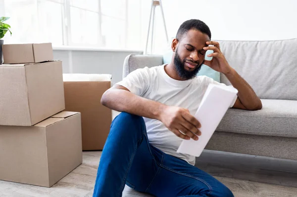 Frustrierter Afrikaner liest Bill, der im Haus zwischen Umzugskartons sitzt — Stockfoto