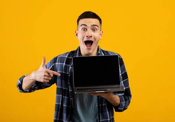 Heyecanlı beyaz adam, turuncu stüdyo arka planında web sitesi tasarımı için boş laptop ekranını işaret ediyor. — Stok fotoğraf