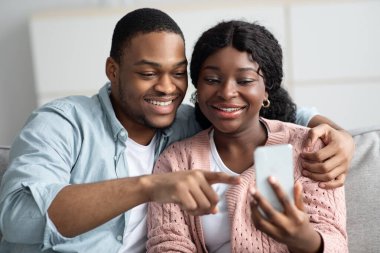 Mutlu siyah eş, kocasına akıllı telefondan fotoğraf gösteriyor.