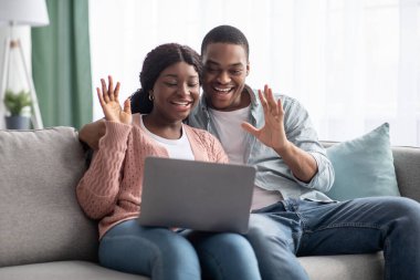 Neşeli siyah çift dizüstü bilgisayara el sallıyor, ev içi.