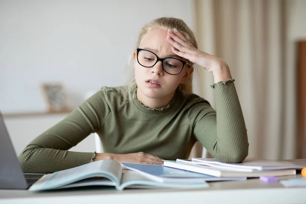 Sad school girl sitting with books at home