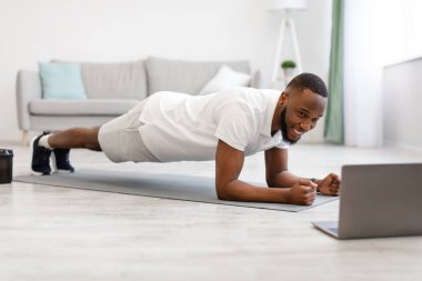 Siyah adam dizüstü bilgisayarda duruyor. Evinde egzersiz yapıyor.